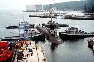 Naval Submarine Base Bangor with tug Mishawaka (rear left) and three other Natick-class tugs guiding the USS&nbsp;Ohio&nbsp;(SSGN-726) out of dry dock at Delta Pier
