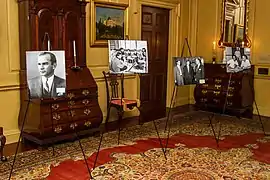 Photographs on display in front of a Bombé desk in the Benjamin Franklin State Dining Room