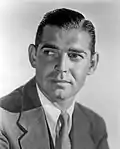 Black and white publicity photo of Clark Gable—a middle-aged white man with a mustache and straight gray hair combed to the side, wearing a suit and smiling—in 1940.