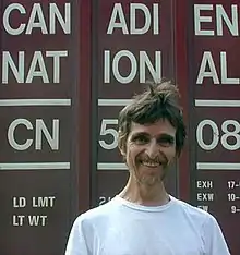 A man wearing a white t-shirt stands with the words "Canadien National" visible behind him.