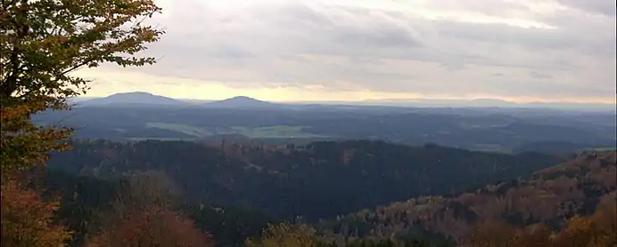View of the Gleichberge (679 and 641 m), 24&nbsp;km away. Right in the background is the High Rhön with the 928-m-high Kreuzberg 67&nbsp;km away, immediately in front (centre half right) the 7-km-distant Ratscher Bergsee. In the foreground is the 621-m-high, Wachberg, 3&nbsp;km away