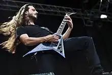 Close-up of Christian Andreu, long hair flying, playing a guitar with a cutaway bottom