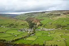 A high level view of a small village set in a low green valley, with moorland beyond