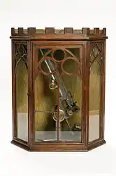 A stand microscope created by Joseph Gutteridge, a weaver from Coventry. The microscope allows coarse and fine adjustments, and its height is adjustable by a set screw. It consists of two objectives each with a screw on cap and a slidecarrier that is moveable laterally. The mirror also has a cap. It has a bench magnifier, lens moveable through 360° and has a base weighted with lead. It is placed in a Mahogany box containing seventeen six-compartment trays of slides.