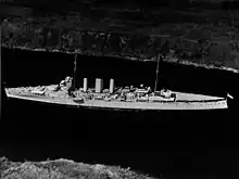 Aerial photograph of a cruiser-size warship sailing slowly through a narrow body of water