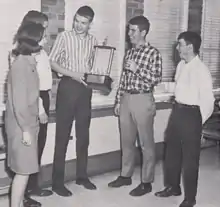 Photograph of high school debaters standing with a trophy