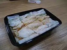 Handmade rice noodle rolls in a black box on a wooden table