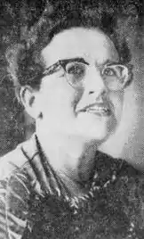 A white woman's face, wearing glasses, short curly hair.