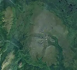 An overhead view of vegetated terrain with two very large, rocky mountains near the crest of a mountain range to the southwest.