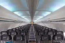 Cabin of the 757. There are six seats per row, with a single aisle separating the seats. Light shines through the side-wall windows and overhead lighting
