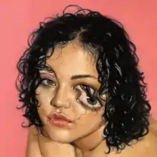 The head of an olive-skinned woman with short curly hair is shown, amidst a pink background. Her eyes are partially distorted, with visual effects used to create a second pair of eyes and a crack directly underneath her right eye, following down to her lips.