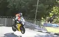 Hervé Gantner wearing a orange high-visibility vest riding a motorcycle on Ballaugh Bridge