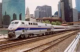 A gray diesel locomotive with a blue stripes and two thinner red stripes on the side. The stripes narrow and angle downwards on the front.