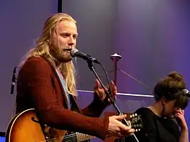 Two members of the band seen sitting onstage, playing their respective instruments