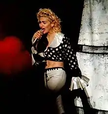 Madonna in a polka dotted blouse and white pants singing onstage