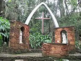 A stone altar with two images of Christian saints in a garden and on it a bow bearing a cross