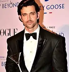 Roshan with a trophy in his hand in a tuxedo as he directly looks at the camera.