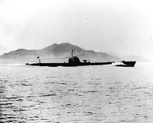 A World War II-era submarine in a body of water with a land mass in the background