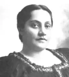 A young Hawaiian woman, dark hair parted center and dressed to the nape, wearing a dark dress with a square ruffled collar