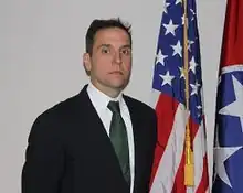 Smith standing in front of flags, wearing a suit