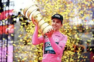 A man wearing a pink jersey while holding a golden trophy.