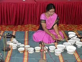Vidushi Shashikala Dani sitting on the ground with water bowls laid out in front of her as she plays music on them
