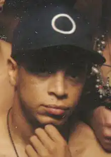 close-up of shirtless black male wearing black cap, one hand to chin