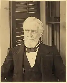 bearded man looking forward with shuttered window in background