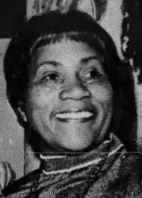 A smiling African-American woman, from a 1977 newspaper. Her hair is cut in bangs, and she is wearing a high-collared blouse.
