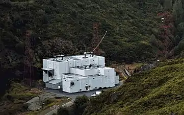 Transmitter building.  From the two bushings on the roof cables supply power to two feed buses which extend both directions along the valley, connected to the overhead antenna wires.