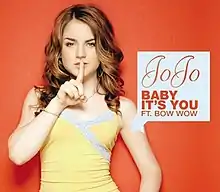 The cover has the artist against an orange background, putting her right index finger to her mouth. Next to the artist is a white box containing the artist's name logo, the song title and the featured artist's name, all colored in orange.
