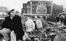 Black and white photograph of Joan Littlewood sat on rubble outside the Theatre Royal, Stratford, East London