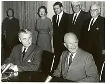 Diefenbaker and a Dwight Eisenhower sit at a table. Two women and three men stand behind them.
