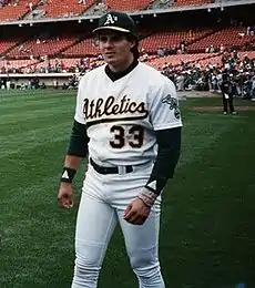 A man in a white baseball uniform and green undersleeves and cap