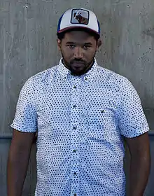 Ammo, wearing a hat and sitting next to a brick wall, eating pizza