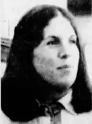 A grainy, black-and-white photo of a white woman with shoulder-length dark hair, looking to the right of the camera