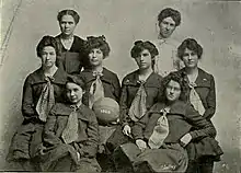 Black-and-white team photo of the 1903 KU women's basketball team with the center-most girl holding a basketball with "1903" painted on it