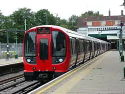 A grey, blue and red S8 stock train waiting at the platform at Croxley station
