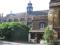 A long, low building of brick and stonework, with arched windows. It is partially obscured by trees and shrubs. The slate roof features a six-sided tower of stone and glass.