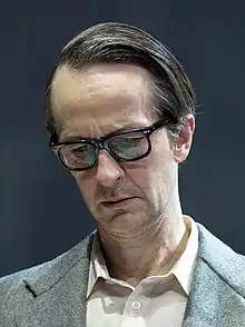 Up-close shot of Caucasian man with combover, wearing glasses, looking down
