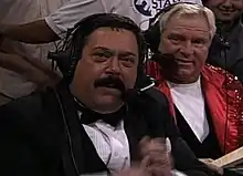 Two men wearing headsets to commentate a professional wrestling event