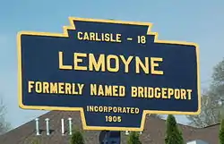 A keystone shaped road marker containing the distance to Carlisle of 18 miles, the name Lemoyne, the description of formerly named Bridgeport, and incorporated 1905.