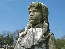 Grey stone statue of a 12-year-old girl with shoulder-length hair.