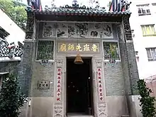 The exterior of a temple, with a large door flanked by Chinese characters. Other urban buildings can be seen in the background.