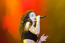 Lorde performing onstage against a background mixing shades of red and orange
