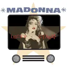Madonna with hands folded and looking towards the front. She has unkempt hair and wears heavy makeup, and a number of junk jewellery on her neck and hands.