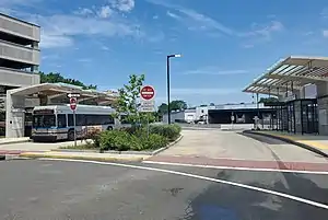 A silver bus at a bus station with angular concrete shelters