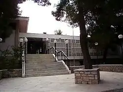 White building with stairs and a tree front of the entrance