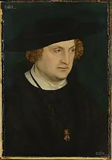 Middle-aged man in black, with a large black hat and light brown hair.