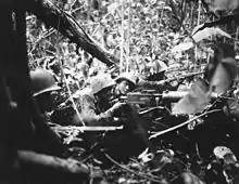 Marines manning a defensive position in the jungle. There is a medium machine gun, as personnel operating individual small arms.
